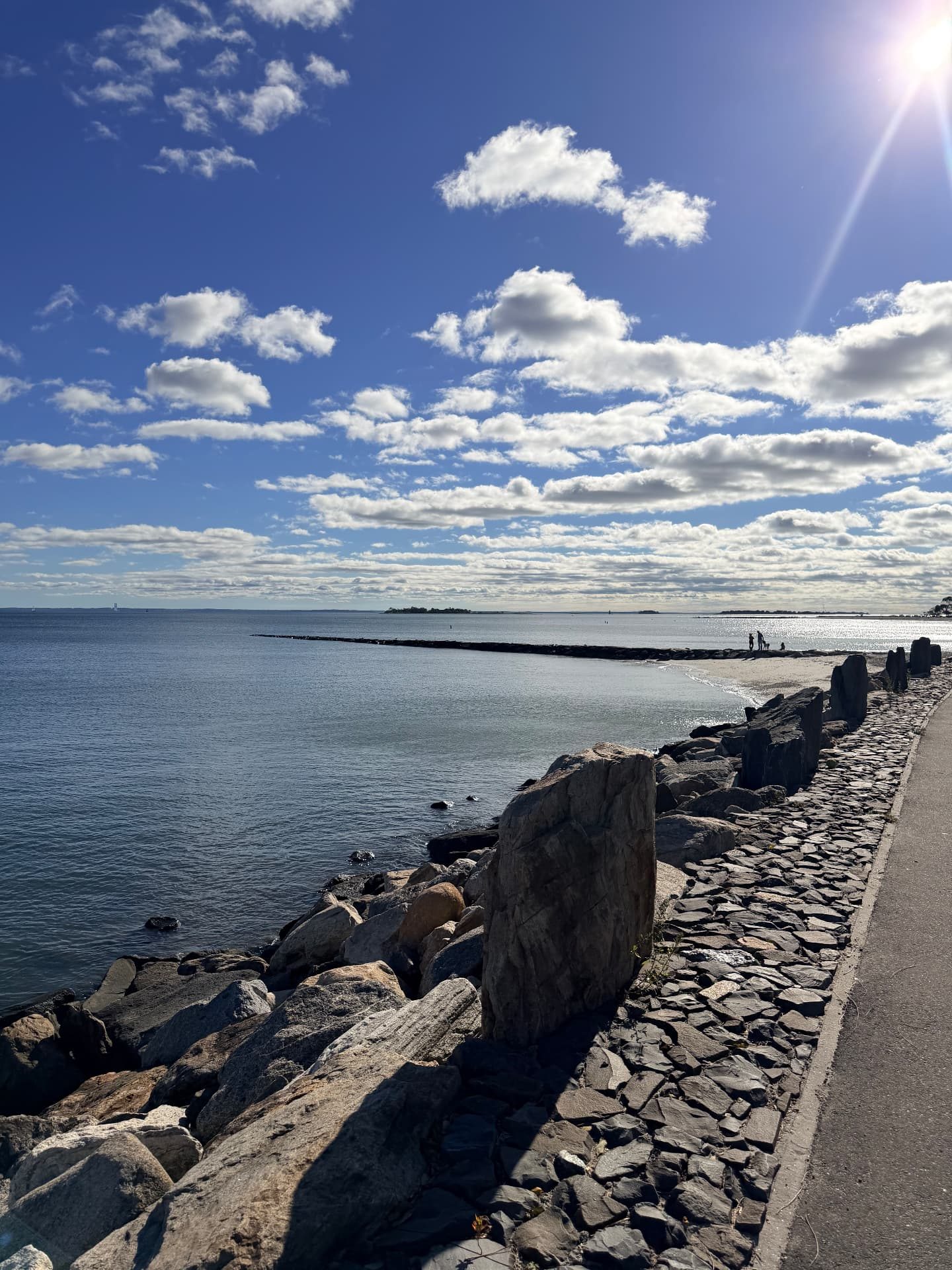 Stone seawall and walkway beside the water with a jetty in the distance